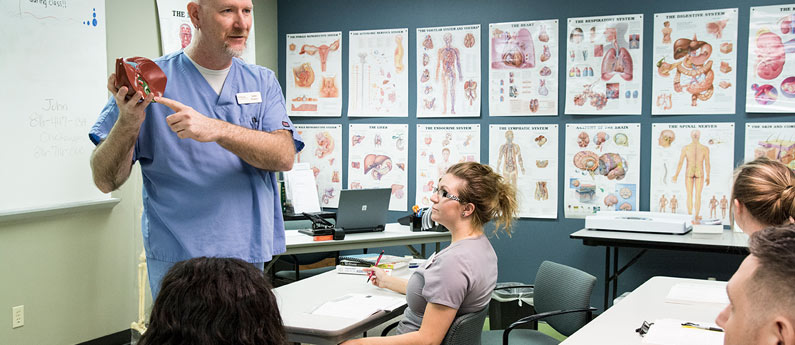 Anatomy teacher at the front of the class with students looking on.