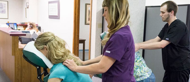 Massage therapists giving clients some chair massages in a clinic setting.