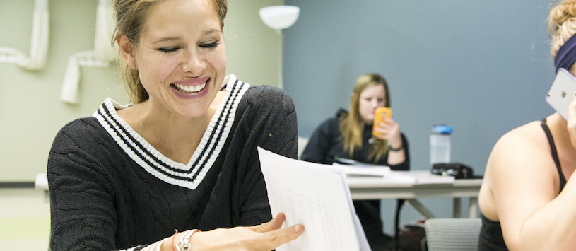 A student smiling and laughing and leafing through a book 