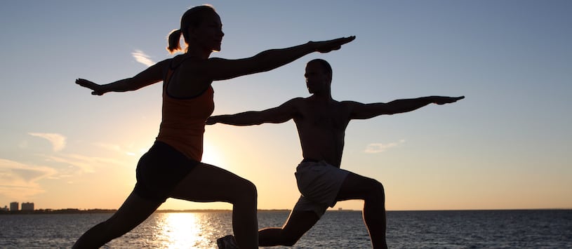 The silhouettes of two people doing yoga against a sunset