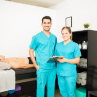 Young physiotherapy professionals with clipboard standing by patient in bed at hospital